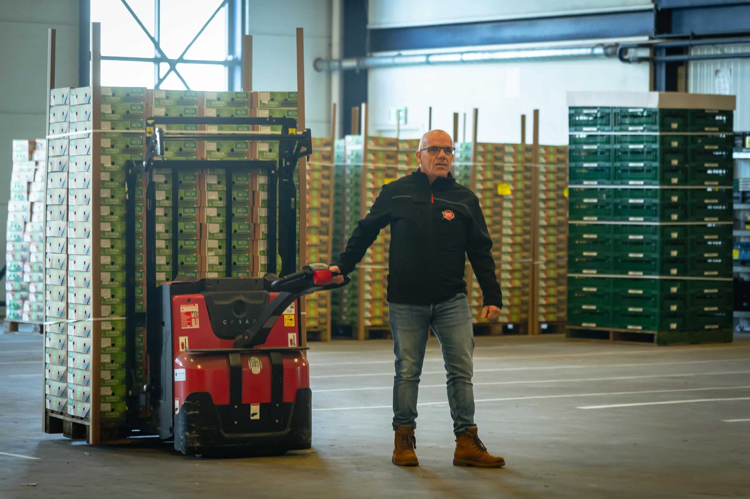 Logistiek medewerker verplaatst transportkarren met elektrische pallettruck in een magazijn vol retourverpakkingen.