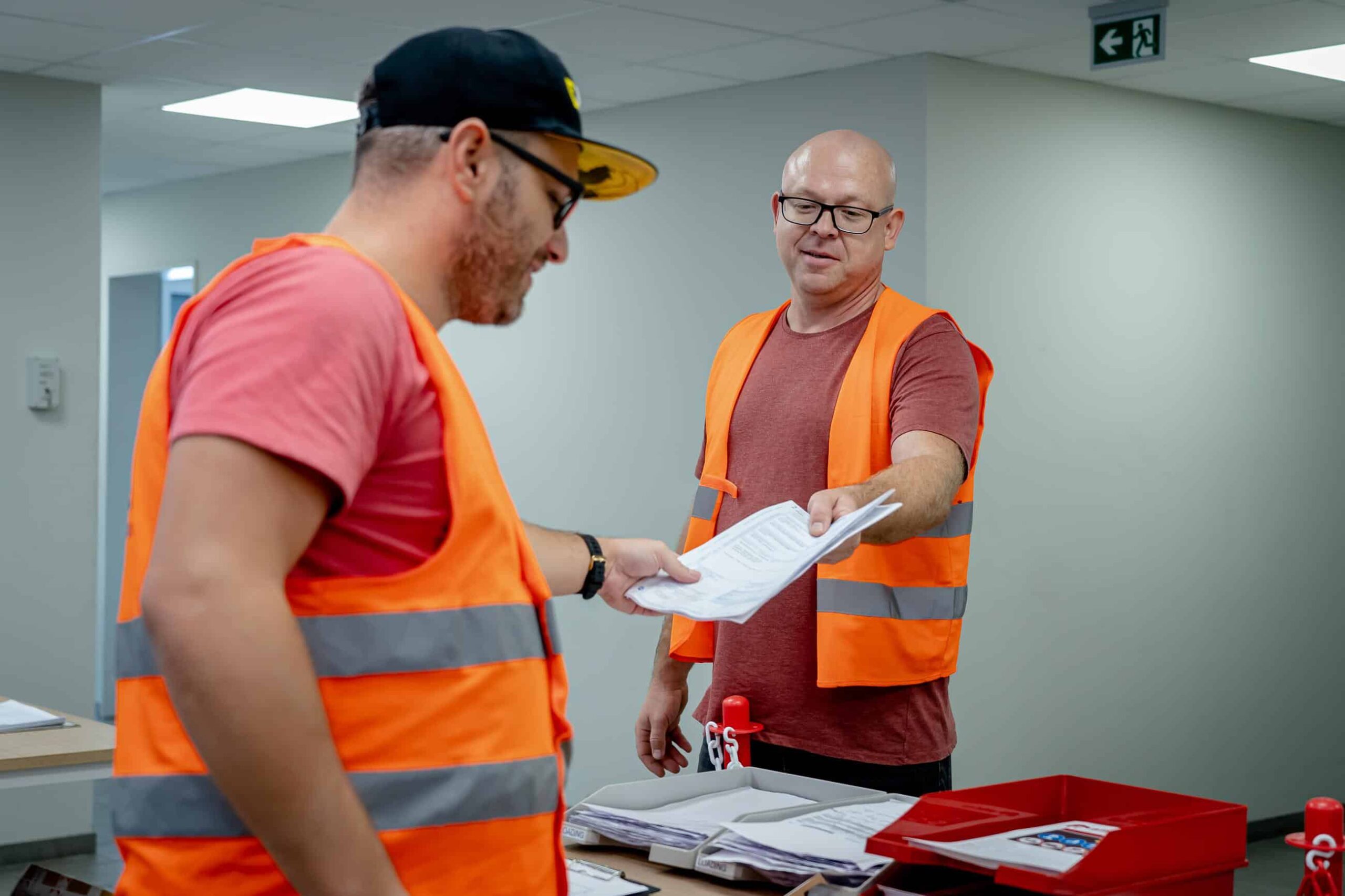 Twee logistiek medewerkers in oranje veiligheidsvesten controleren vrachtpapieren voor luchttransport.