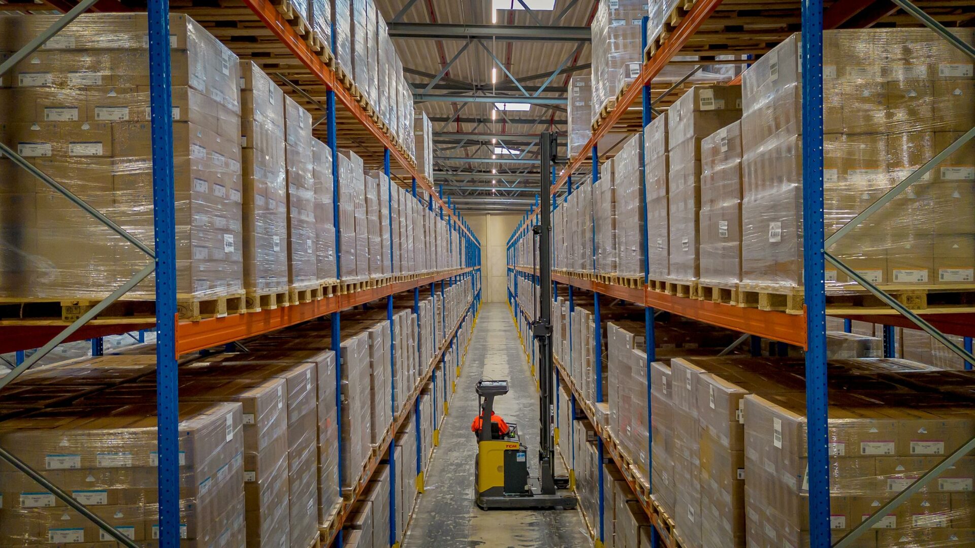 Lange gang met hoge palletstellingen en een heftruck in het Alblas distributiemagazijn.
