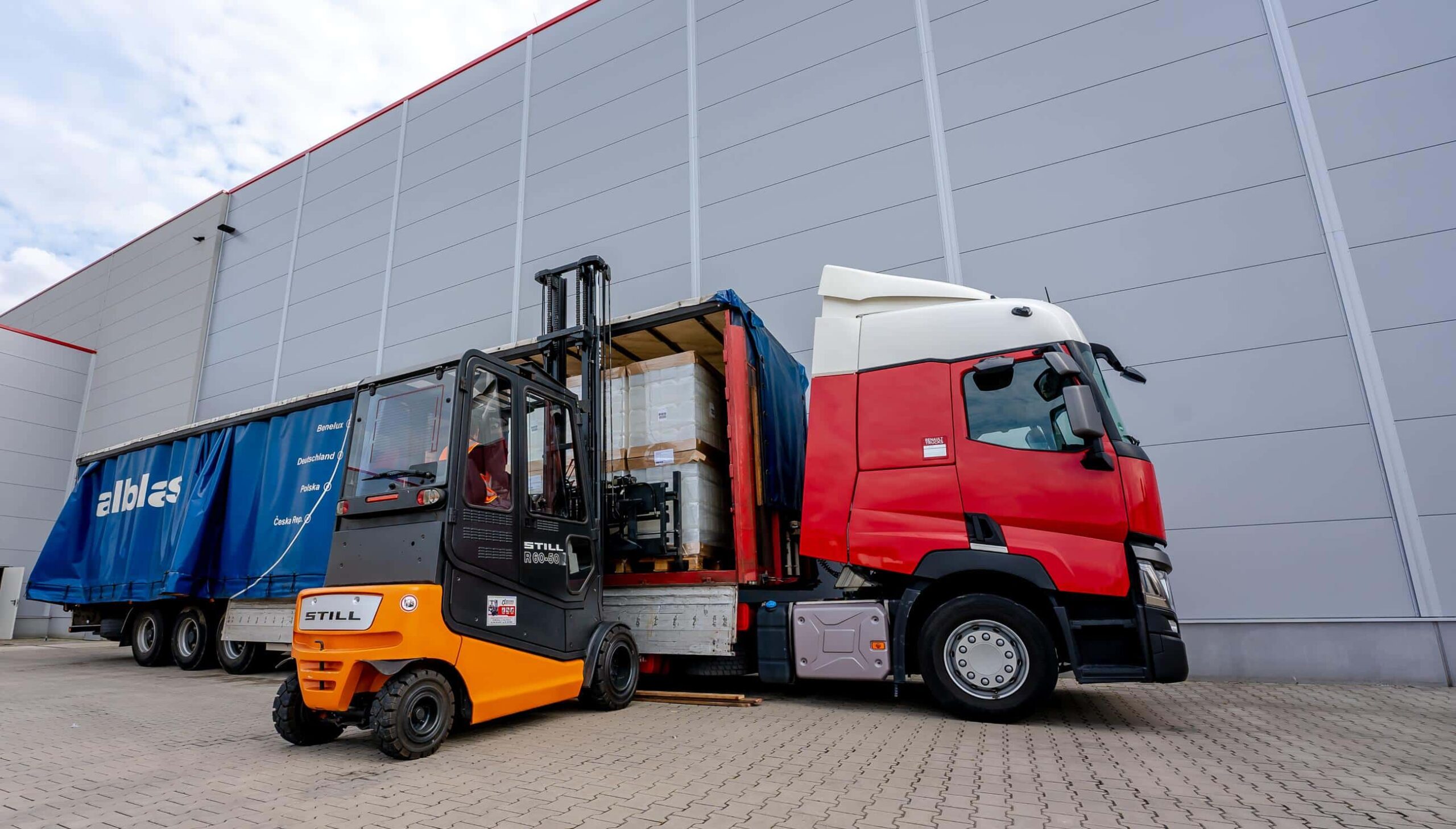 Heftruckchauffeur laadt een rode Alblas-vrachtwagen bij het magazijn voor een nieuwe klant.