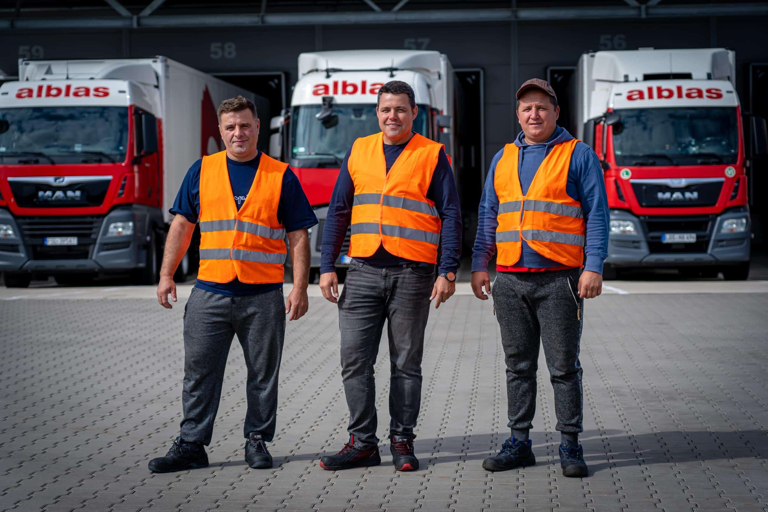 Drie Alblas-chauffeurs in oranje veiligheidsvesten poseren voor vrachtwagens bij de locatie in ’s-Gravendeel.