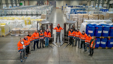 Team van transportbedrijf Alblas op de locatie Emsbüren, poserend in het magazijn tussen pallets en heftrucks.